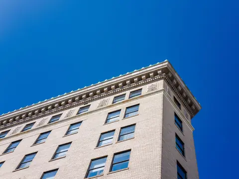 A pale brick building's long cornice against a deep blue sky