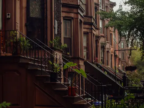 A street of brownstone rowhouses with stoops and trees