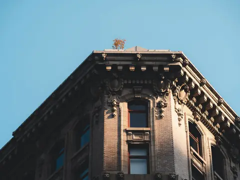 The carved cornice of an old stone and brick corner building against a blue sky