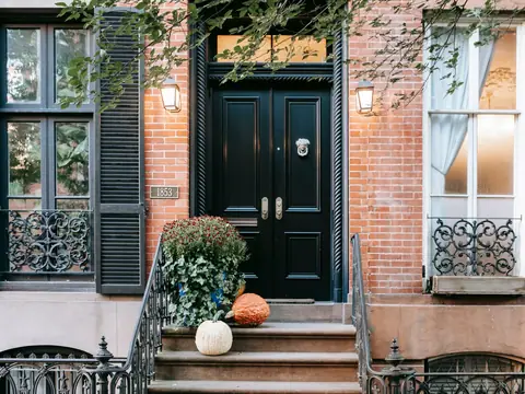 A rowhouse stoop and black front door between tall windows