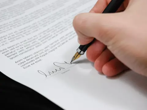 A hand signing a written contract with a fountain pen