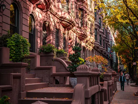 A block of attached brownstone rowhouses with stoops, seen from the sidewalk
