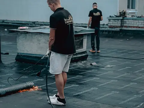 Two roofers on a flat roof with a torch hose and new membrane