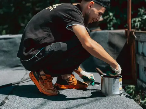 A roofer brushing sealant along a flat roof's edge