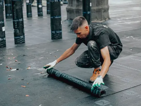 A roofer unrolling a new membrane across a flat roof