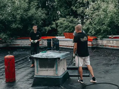 Two roofers at work on a flat roof behind a low parapet