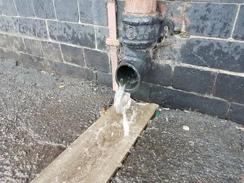 Rainwater pouring from a downspout at the foot of a wall